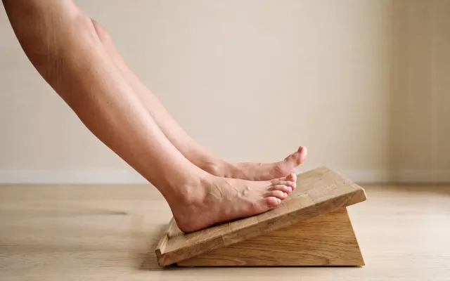 Deux jambes et deux pieds nus posés sur un repose-pieds incliné, orteils légèrement relevés, cadrés sous le bureau.