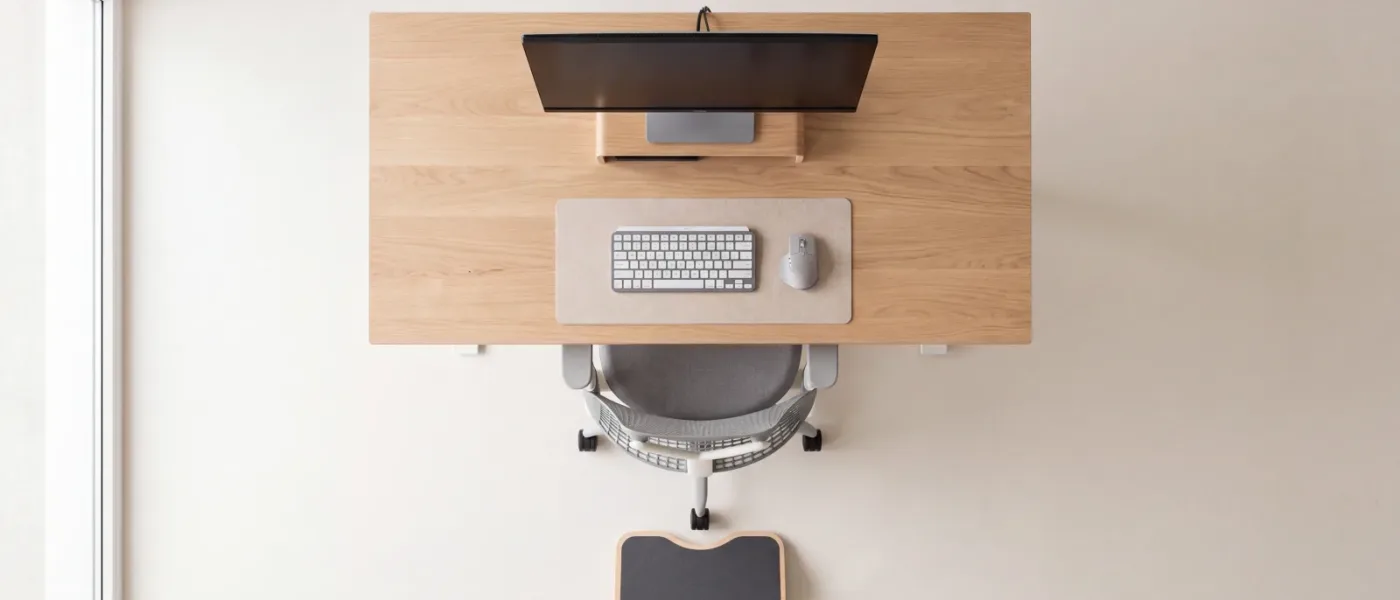 Un poste de travail vu de dessus à la verticale : bureau en bois clair, clavier, siège glissé dessous et repose-pieds posé au sol.