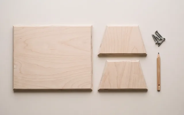 Trois pièces de contreplaqué clair posées à plat vues de dessus, une plaque rectangulaire et deux joues en trapèze, avec des vis et un crayon de menuisier.