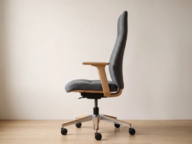 Un siège de bureau vide vu de profil, dont l'assise en tissu gris est légèrement creusée sur son tiers avant.